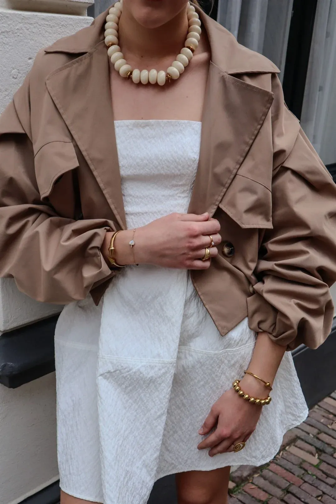 Model in een camel trenchcoat met grote houten kralenketting